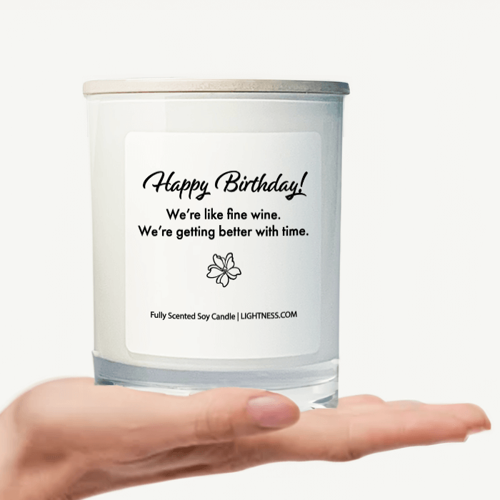 Candle in white glass jar on hand with birthday quote - Happy Birthday! We're like fine wine. We're getting better with time.