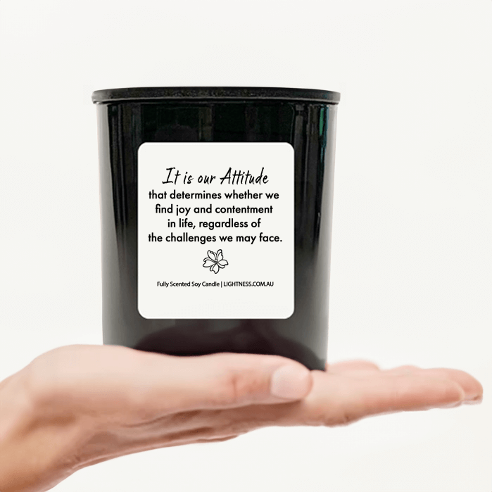 Candle in black glass jar on hand with Happiness quote - It is our attitude that determines whether we find joy and contentment in life, regardless of the challenges we may face.