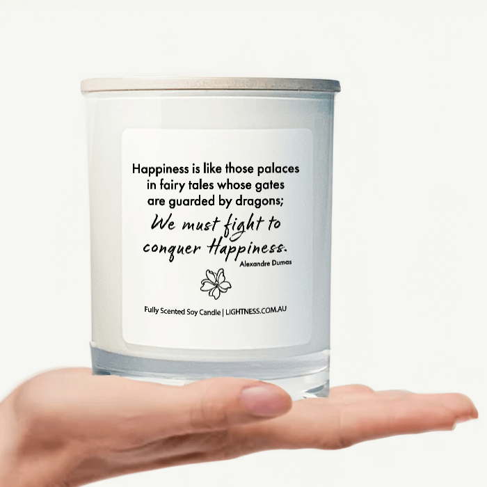 Candle in white glass jar on hand with Happiness quote - Happiness is like those palaces in fairy tales whose gates are guarded by dragons; we must fight in order to conquer it.