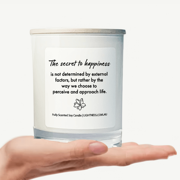 Candle in white glass jar on hand with Happiness quote - The secret to happiness is not determined by external factors, but rather by the way we choose to perceive and approach life.