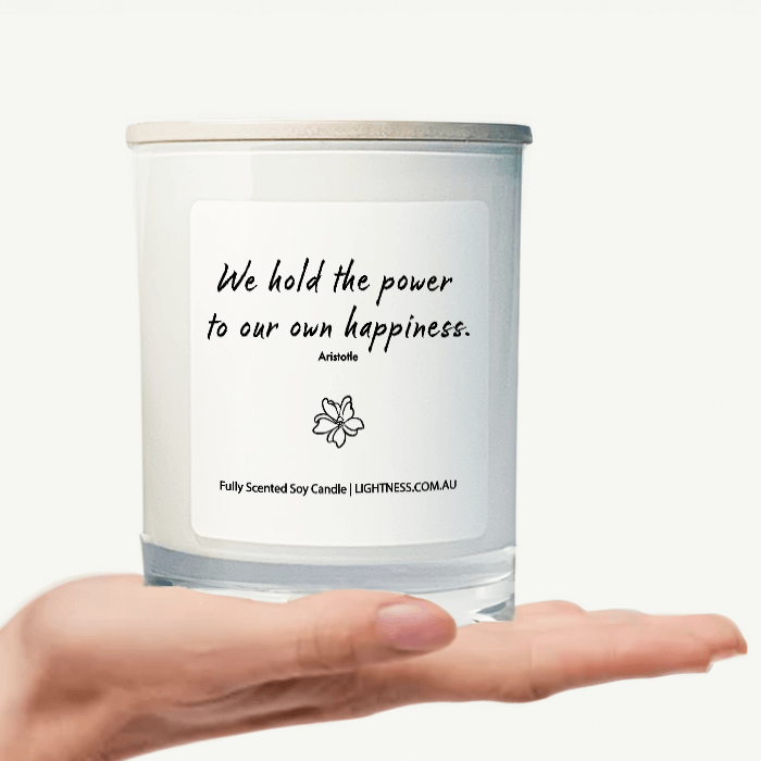 Candle in white glass jar on hand with Happiness quote - We hold the power to our own happiness.