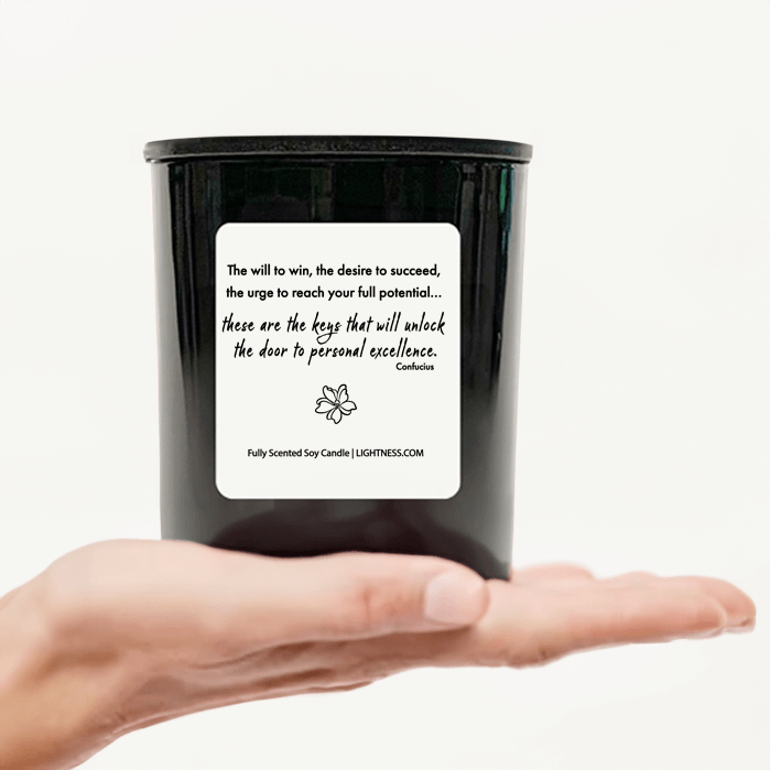 Candle in black glass jar on hand with motivational quote - The will to win, the desire to succeed, the urge to reach your full potential... these are the keys that will unlock the door to personal excellence.