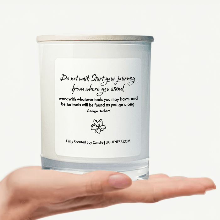 Candle in white glass jar on hand with motivational quote - Do not wait; Start your journey from where you stand, work with whatever tools you may have, and better tools will be found as you go along.