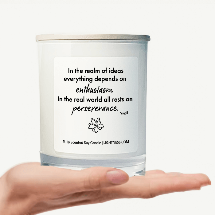 Candle in white glass jar on hand with motivational quote - In the realm of ideas everything depends on enthusiasm. In the real world all rests on perseverance.