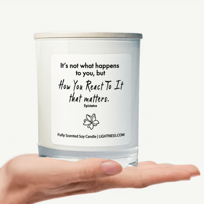 Candle in white glass jar on hand with motivational quote - It's not what happens to you, but how you react to it that matters.