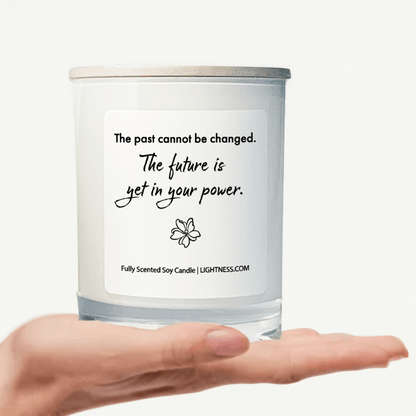 Candle in white glass jar on hand with motivational quote - The past cannot be changed. The future is yet in your power.