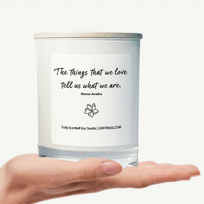 Candle in white glass jar on hand with motivational quote - The things that we love tell us what we are.