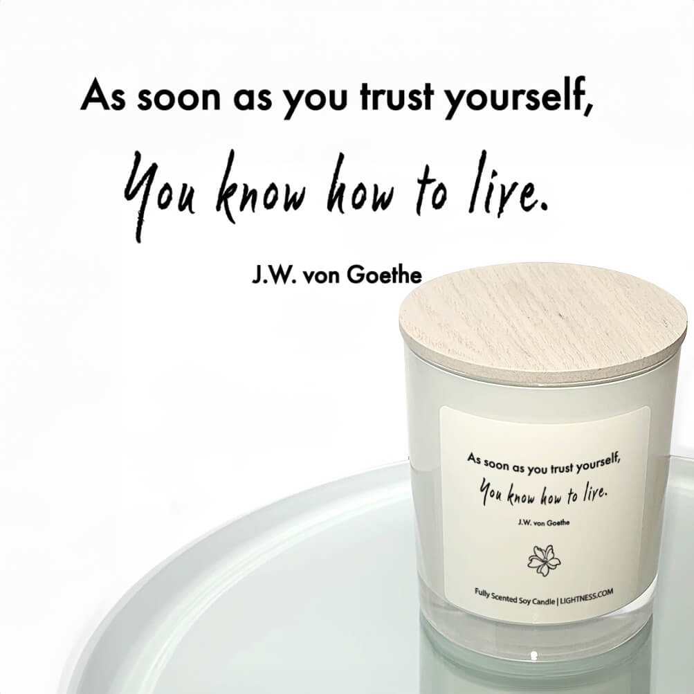 Candle in white glass jar reflected in mirror with motivational quote - As soon as you trust yourself, you know how to live.