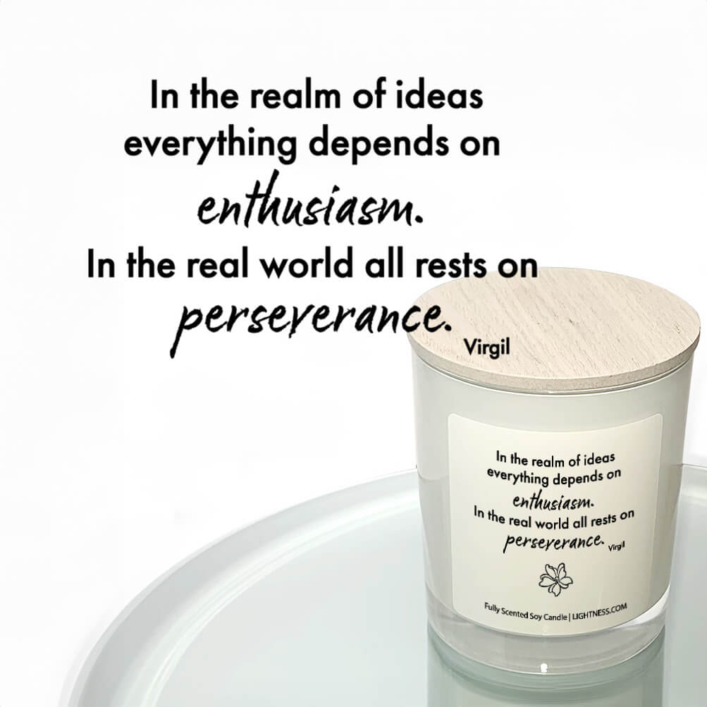 Candle in white glass jar reflected in mirror with motivational quote - In the realm of ideas everything depends on enthusiasm. In the real world all rests on perseverance.