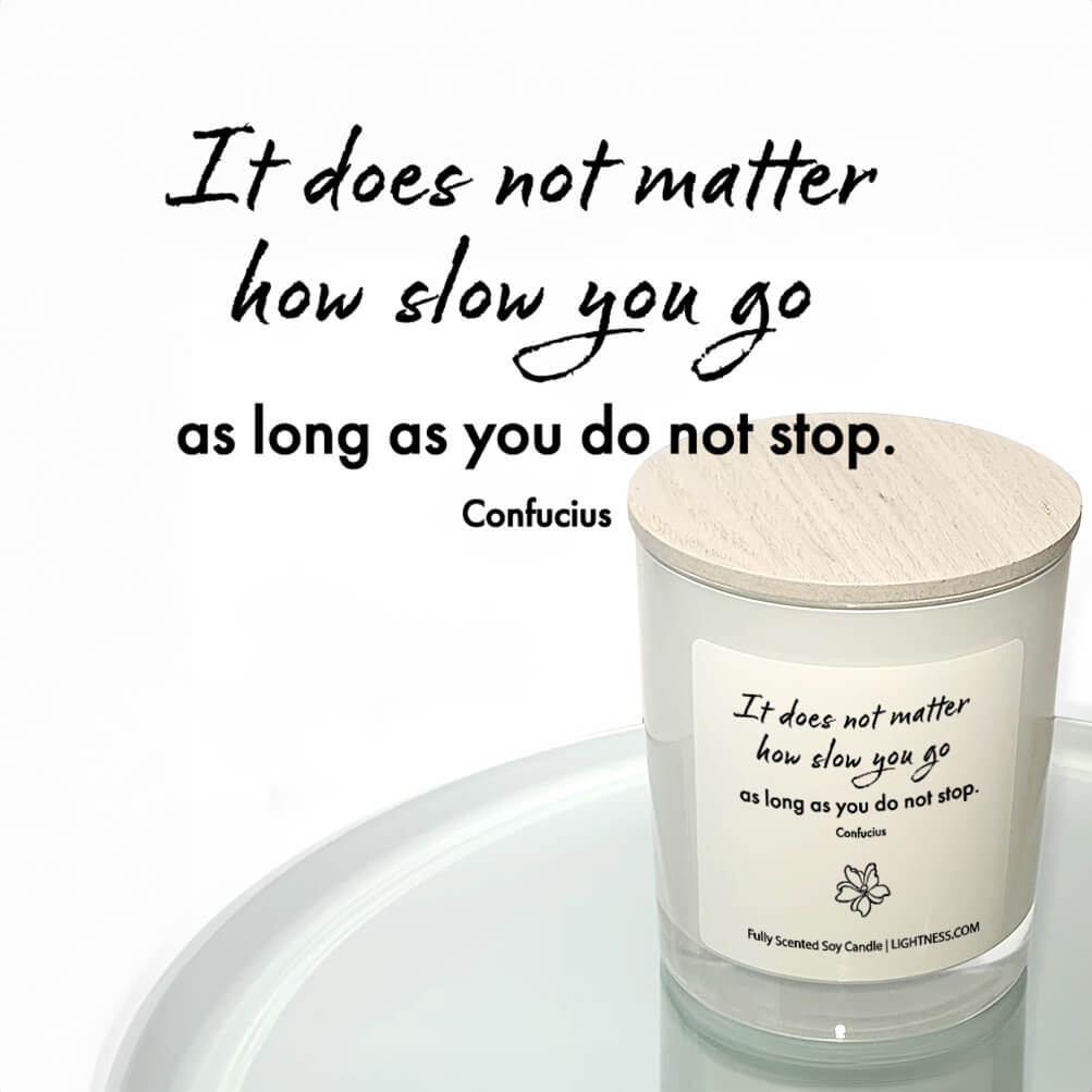 Candle in white glass jar reflected in mirror with motivational quote - It does not matter how slow you go as long as you do not stop.